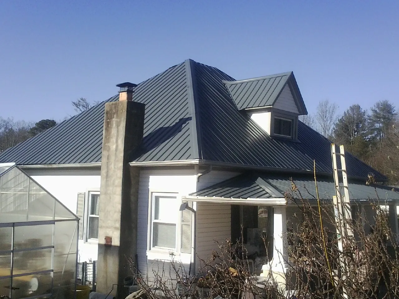 Dark blue standing seam metal roof on a white farmhouse with dormer — Slate & Tile Roof Repair by Roofing Brothers in Radcliffe