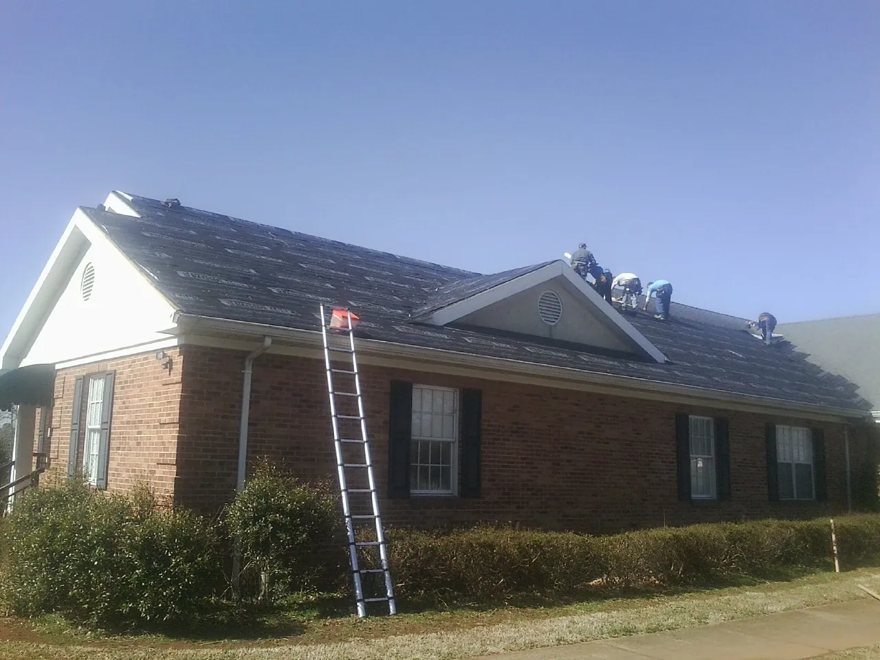 Crew tearing shingles off a brick ranch roof with a ladder set — Emergency Roof Repair work by our crew in Radcliffe