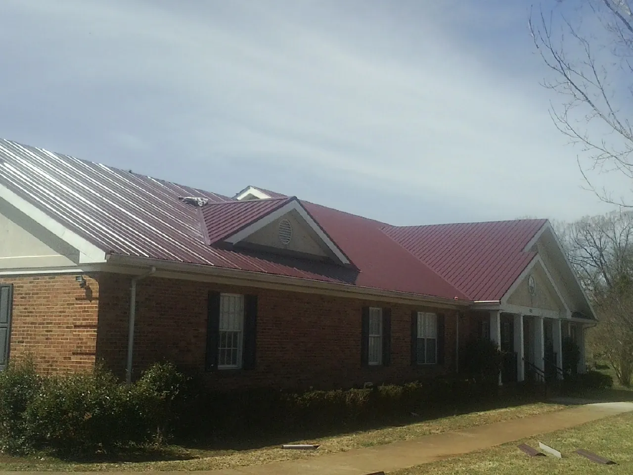 Red metal roof with gabled entries on a long brick building, from a Hail Damage Roof Repair job in Radcliffe