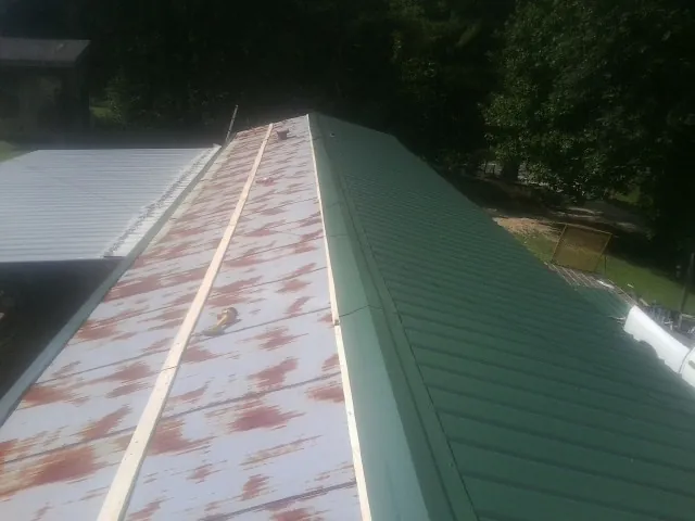 Old rusted panels beside newly installed green metal roofing — Wind Damage Roof Repair by Roofing Brothers in Radcliffe