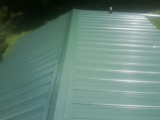 New green metal panels meeting at the ridge of a roof — Flat Roof Repair work by our crew in Radcliffe