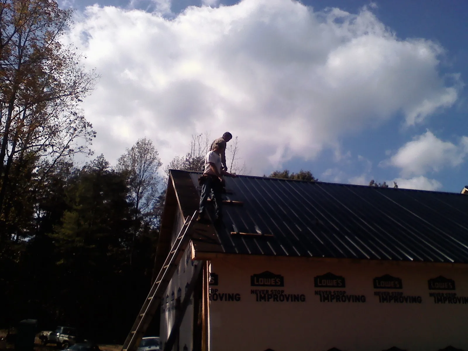 Roofer fastening dark metal panels high against a cloudy sky, from a Roof Inspection job in Radcliffe